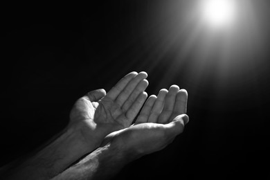Image of Man illuminated by holy light praying in darkness, closeup. Black-and-white effect