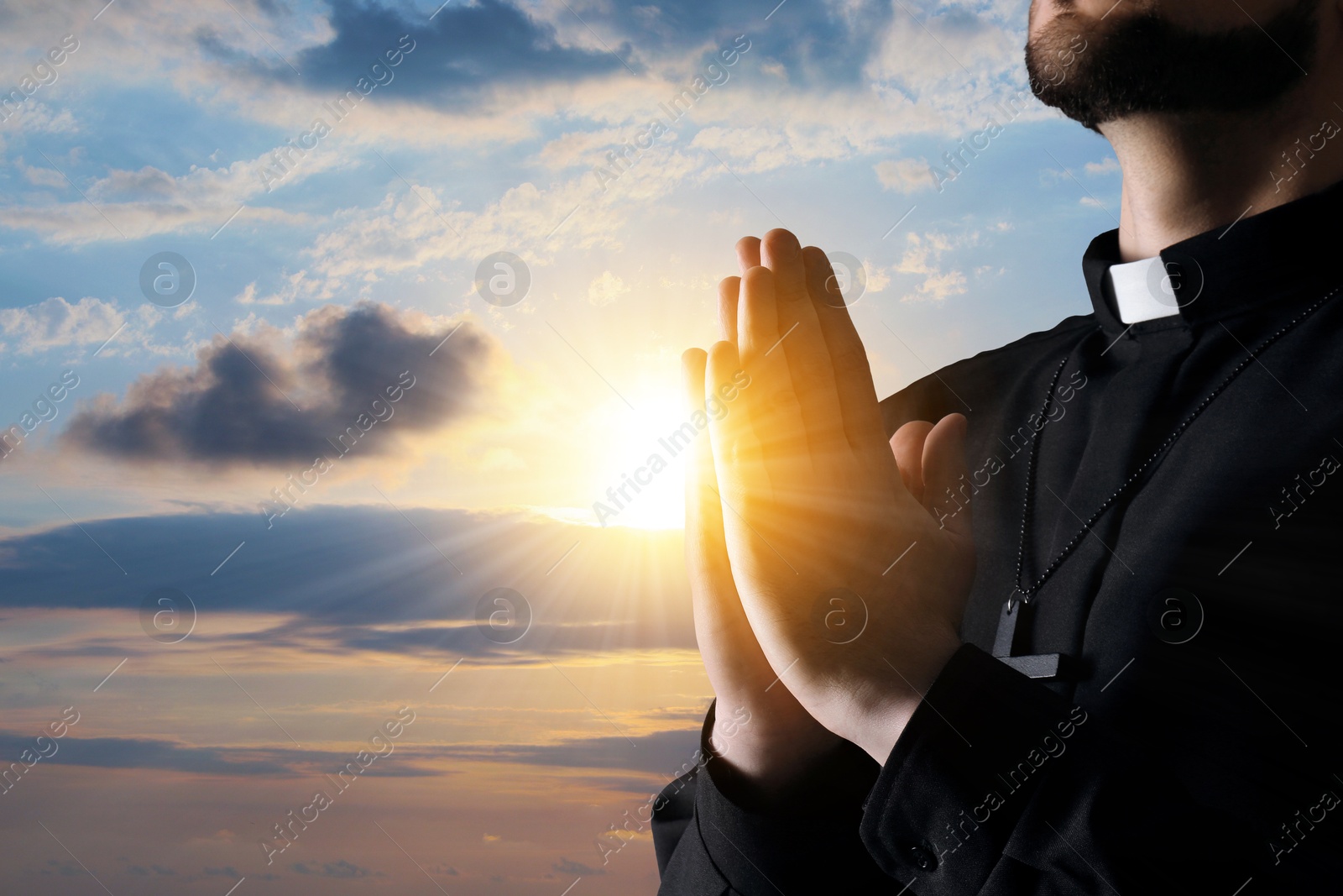 Priest praying against beautiful sunset sky, closeup Image of Priest praying against beautiful sunset sky, closeup