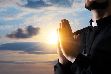 Image of Priest praying against beautiful sunset sky, closeup