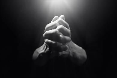 Image of Woman illuminated by holy light praying in darkness, closeup. Black-and-white effect