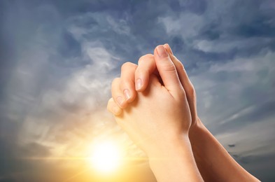 Image of Woman praying against beautiful sky with sun, closeup