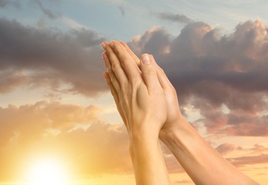 Image of Woman praying against beautiful sky with sun, closeup