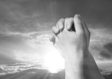 Image of Man praying against beautiful sky with sun, closeup. Black-and-white effect