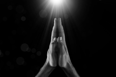 Image of Man illuminated by holy light praying in darkness, closeup. Black-and-white effect
