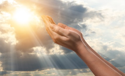 Image of Woman praying against beautiful sky with sun, closeup