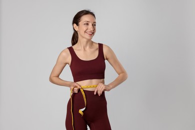 Photo of Beautiful woman measuring her belly with tape on gray background