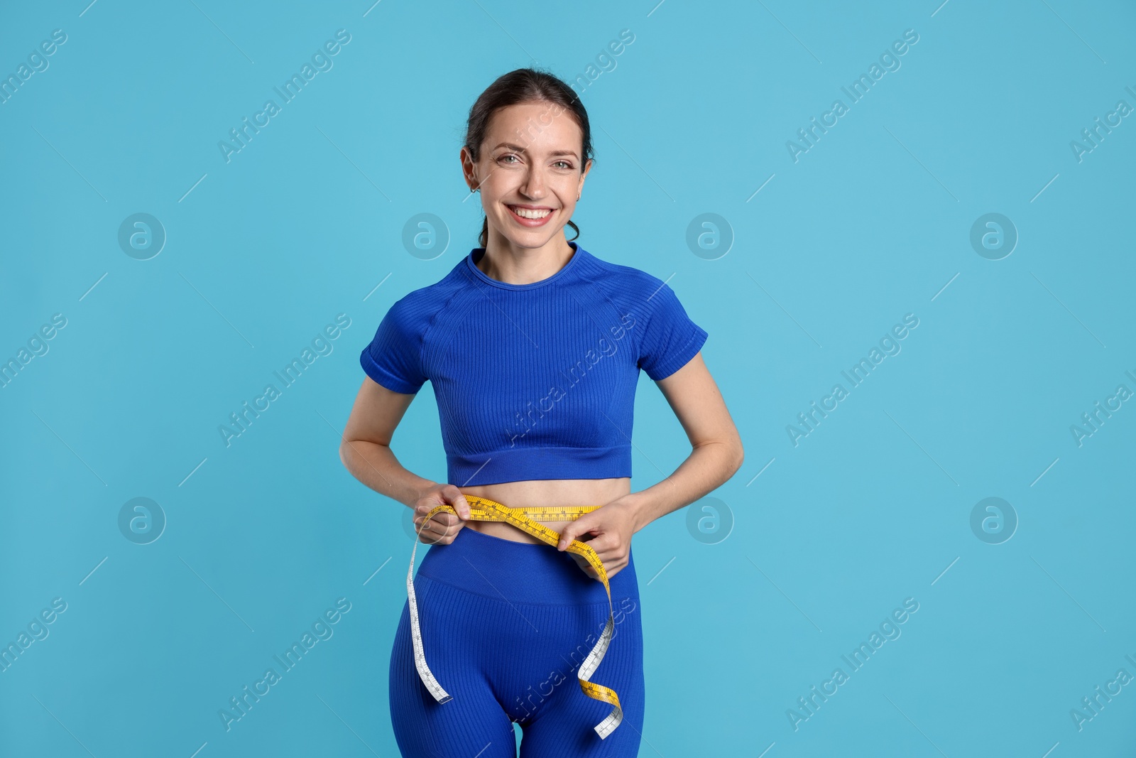 Beautiful woman measuring her belly with tape on light blue background Photo of Beautiful woman measuring her belly with tape on light blue background