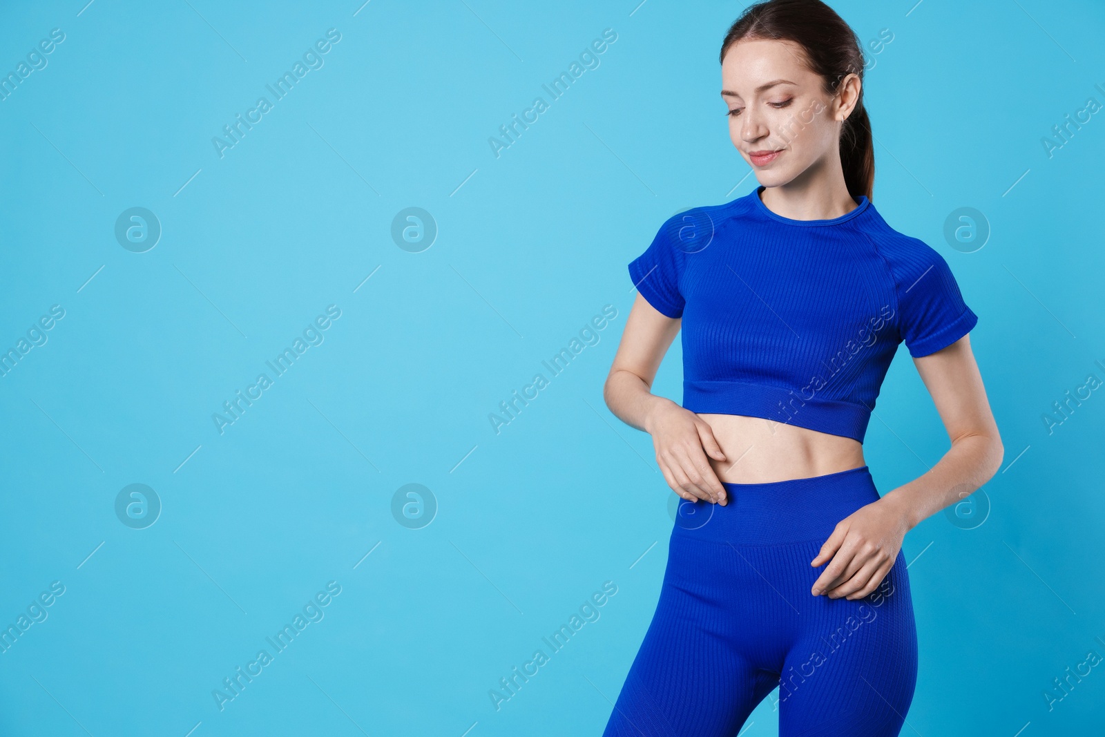 Beautiful woman with flat belly on light blue background, space for text Photo of Beautiful woman with flat belly on light blue background, space for text
