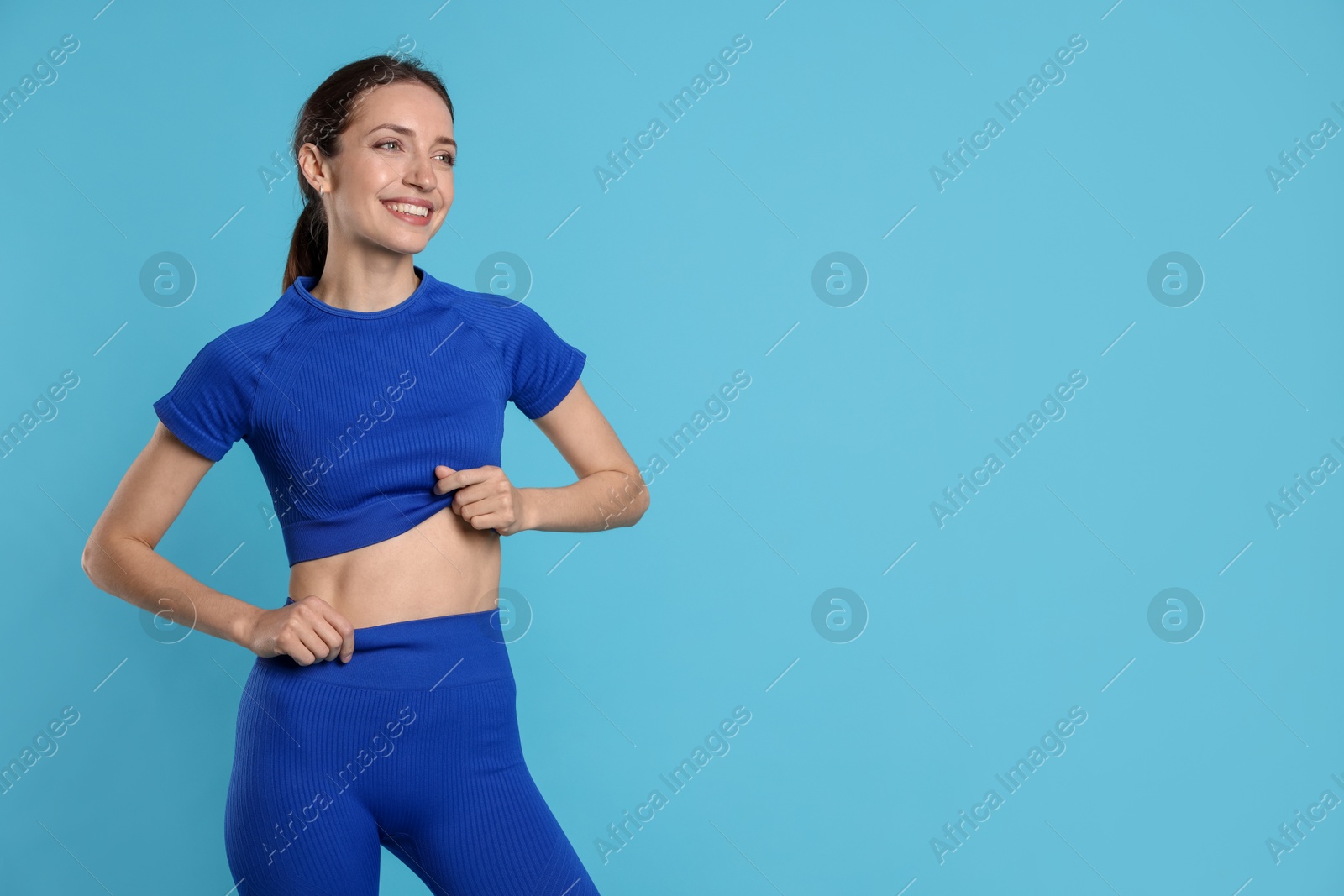 Beautiful woman with flat belly on light blue background, space for text Photo of Beautiful woman with flat belly on light blue background, space for text