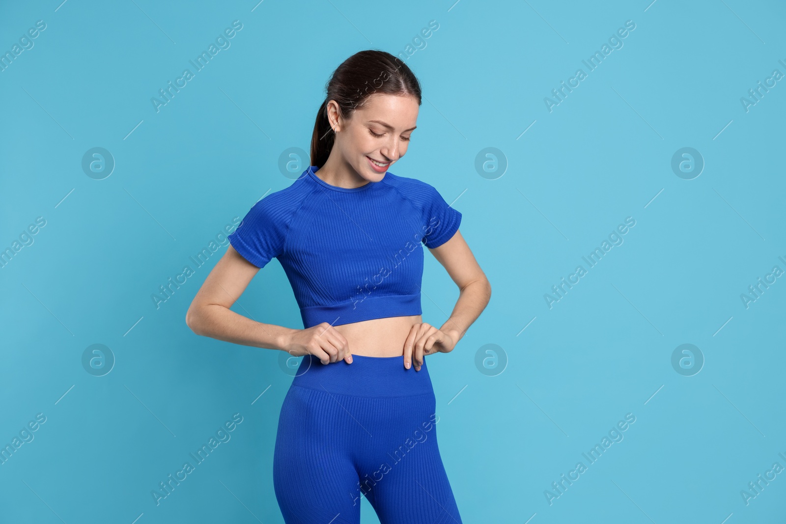 Beautiful woman with flat belly on light blue background Photo of Beautiful woman with flat belly on light blue background