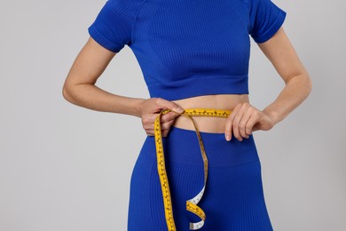 Photo of Woman measuring her belly with tape on gray background, closeup