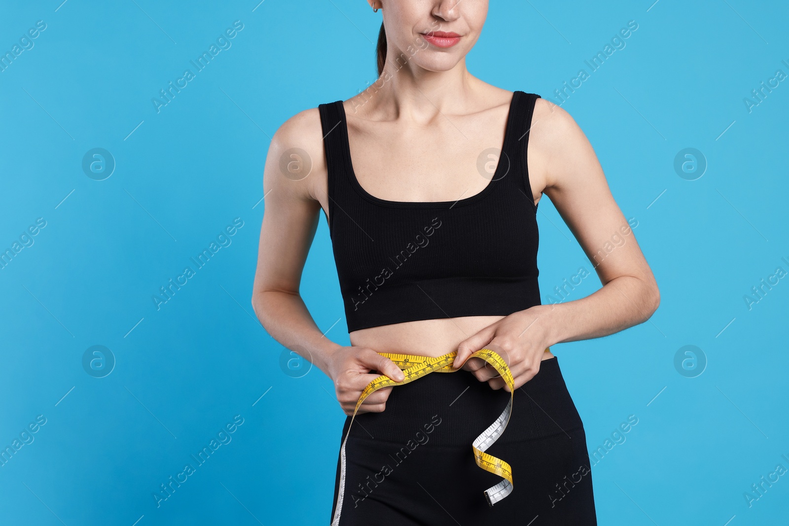 Woman measuring her belly with tape on light blue background, closeup. Space for text Photo of Woman measuring her belly with tape on light blue background, closeup. Space for text