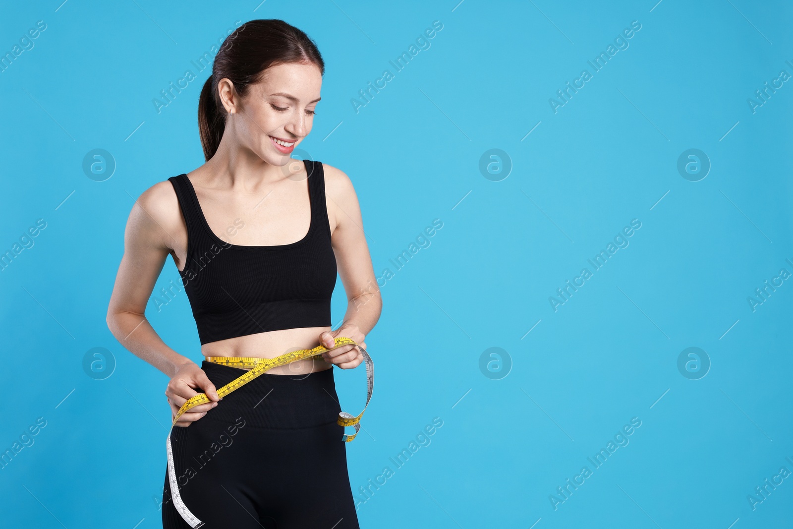 Beautiful woman measuring her belly with tape on light blue background, space for text Photo of Beautiful woman measuring her belly with tape on light blue background, space for text