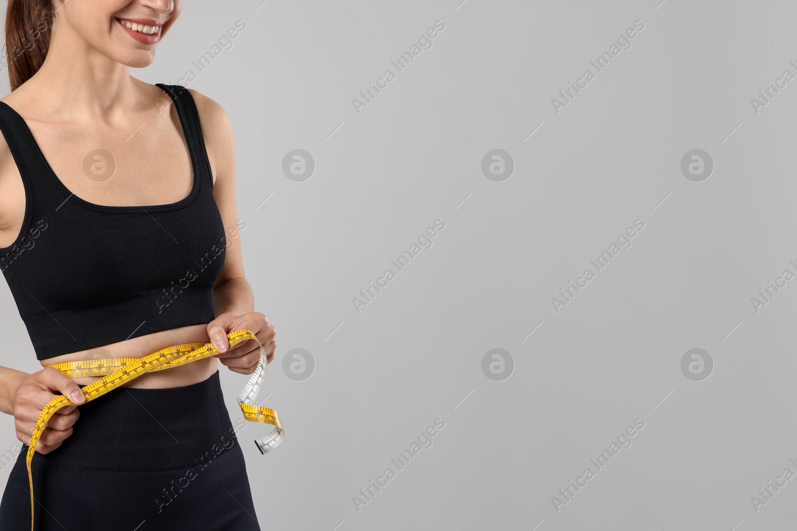 Woman measuring her belly with tape on gray background, closeup. Space for text Photo of Woman measuring her belly with tape on gray background, closeup. Space for text
