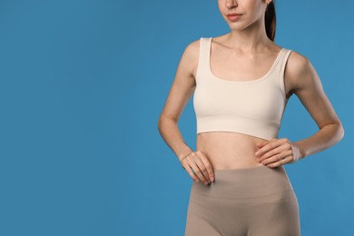 Photo of Beautiful woman with flat belly on light blue background, closeup. Space for text