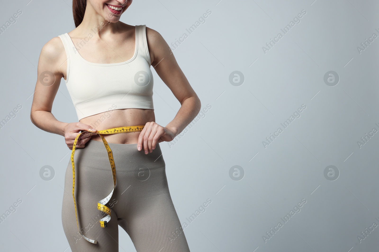 Woman measuring her belly with tape on gray background, closeup. Space for text Photo of Woman measuring her belly with tape on gray background, closeup. Space for text