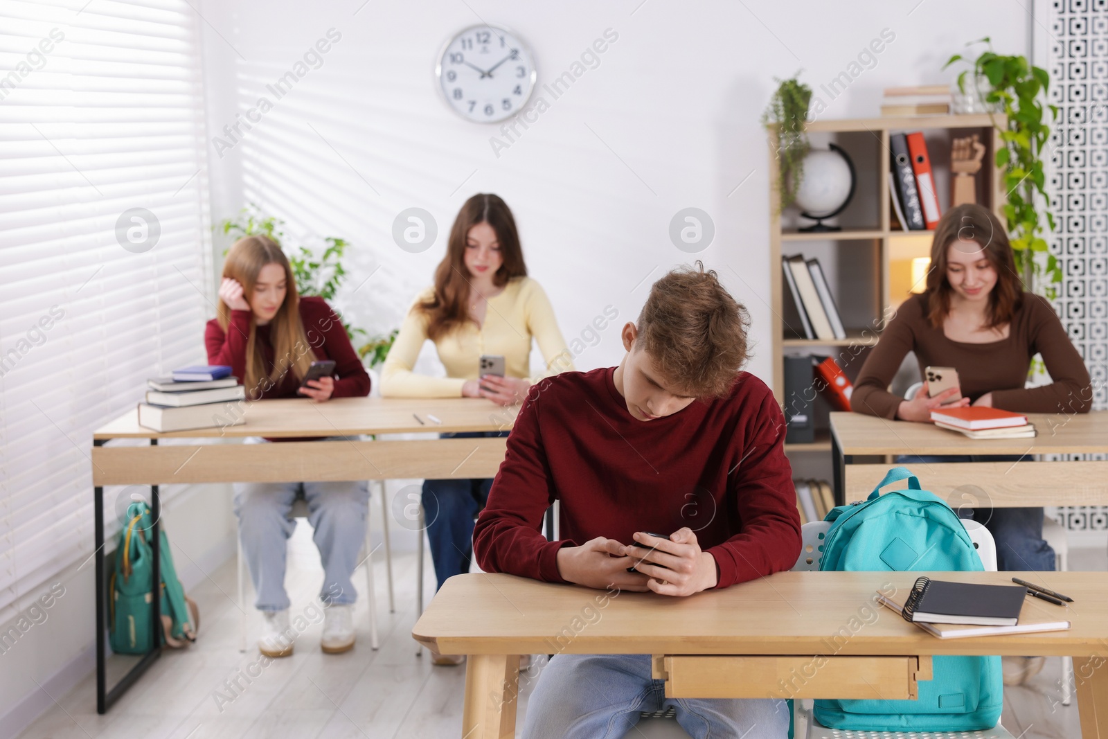 Cyber bullying. Upset teenage boy with smartphone at desk in classroom Photo of Cyber bullying. Upset teenage boy with smartphone at desk in classroom