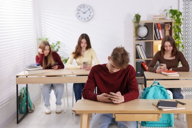 Photo of Cyber bullying. Upset teenage boy with smartphone at desk in classroom
