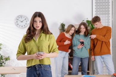 Photo of Teenage girl with smartphone suffering from bullying at school, selective focus
