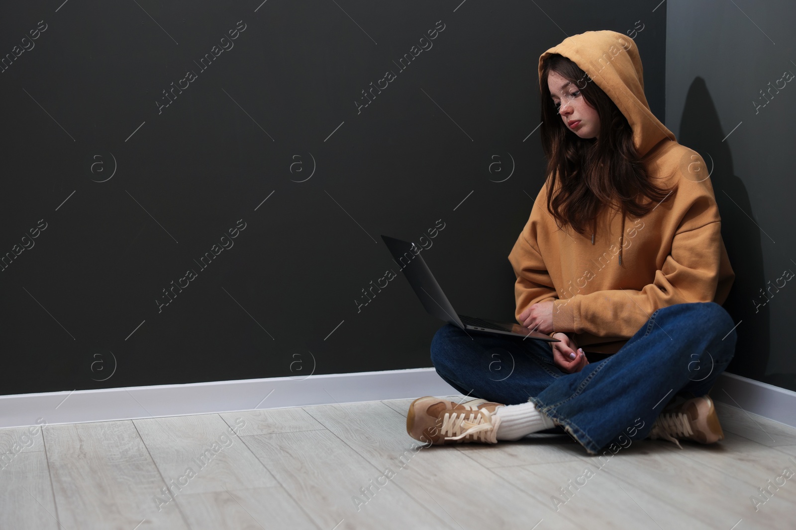 Cyber bullying. Upset teenage girl with laptop on floor indoors. Space for text Photo of Cyber bullying. Upset teenage girl with laptop on floor indoors. Space for text