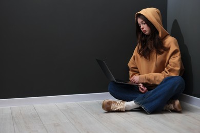 Photo of Cyber bullying. Upset teenage girl with laptop on floor indoors. Space for text