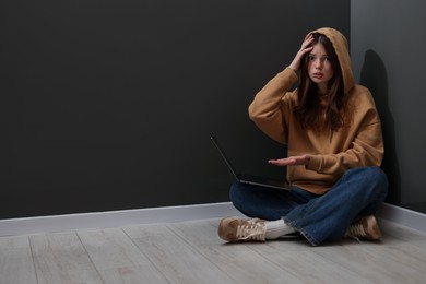 Photo of Cyber bullying. Upset teenage girl with laptop on floor indoors. Space for text