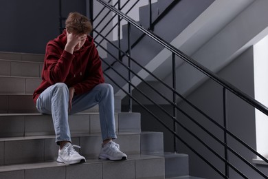 Photo of Bullying. Upset teenage boy on stairs indoors