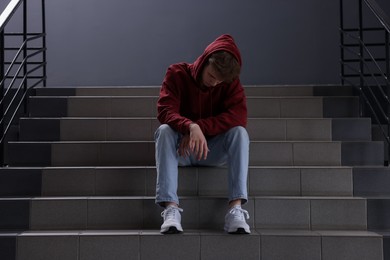 Photo of Bullying. Upset teenage boy on stairs indoors