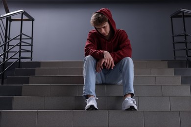 Photo of Bullying. Upset teenage boy on stairs indoors