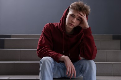 Photo of Bullying. Upset teenage boy on stairs indoors