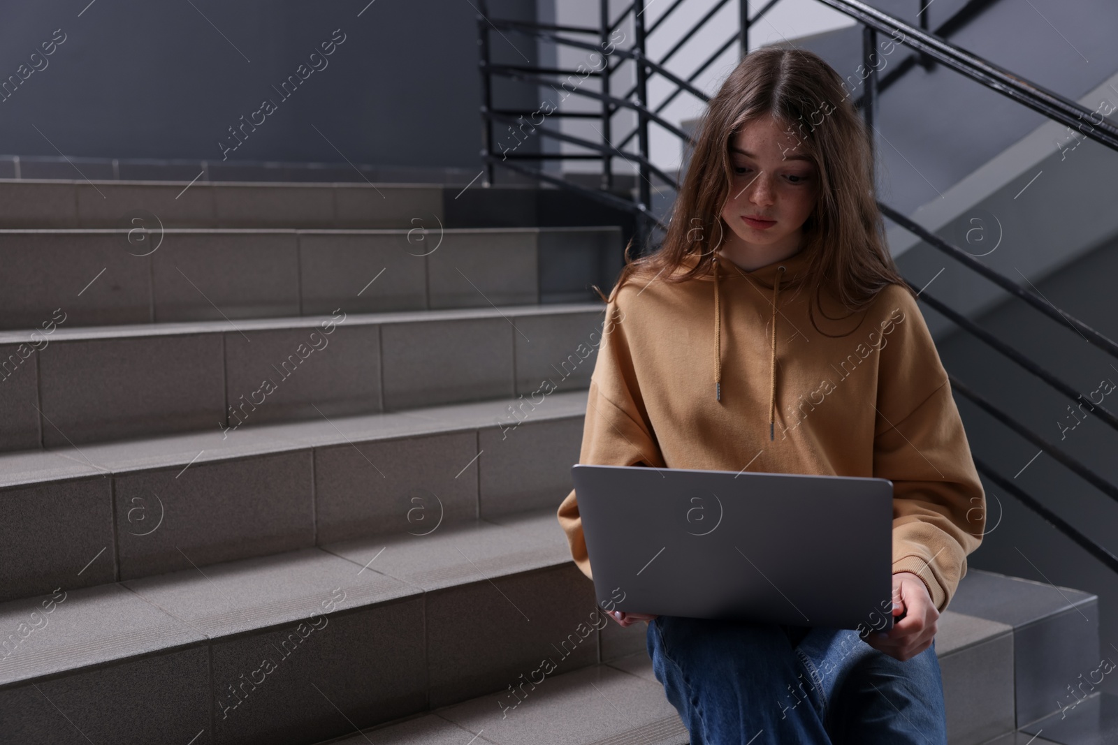 Cyber bullying. Upset teenage girl with laptop on stairs indoors. Space for text Photo of Cyber bullying. Upset teenage girl with laptop on stairs indoors. Space for text