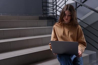 Photo of Cyber bullying. Upset teenage girl with laptop on stairs indoors. Space for text