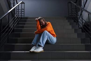 Photo of Bullying. Upset teenage girl on stairs indoors