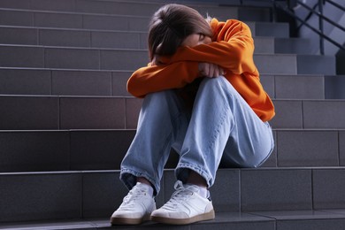 Photo of Bullying. Upset teenage girl on stairs indoors