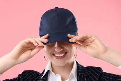 Photo of Smiling woman in stylish baseball hat on pink background, closeup