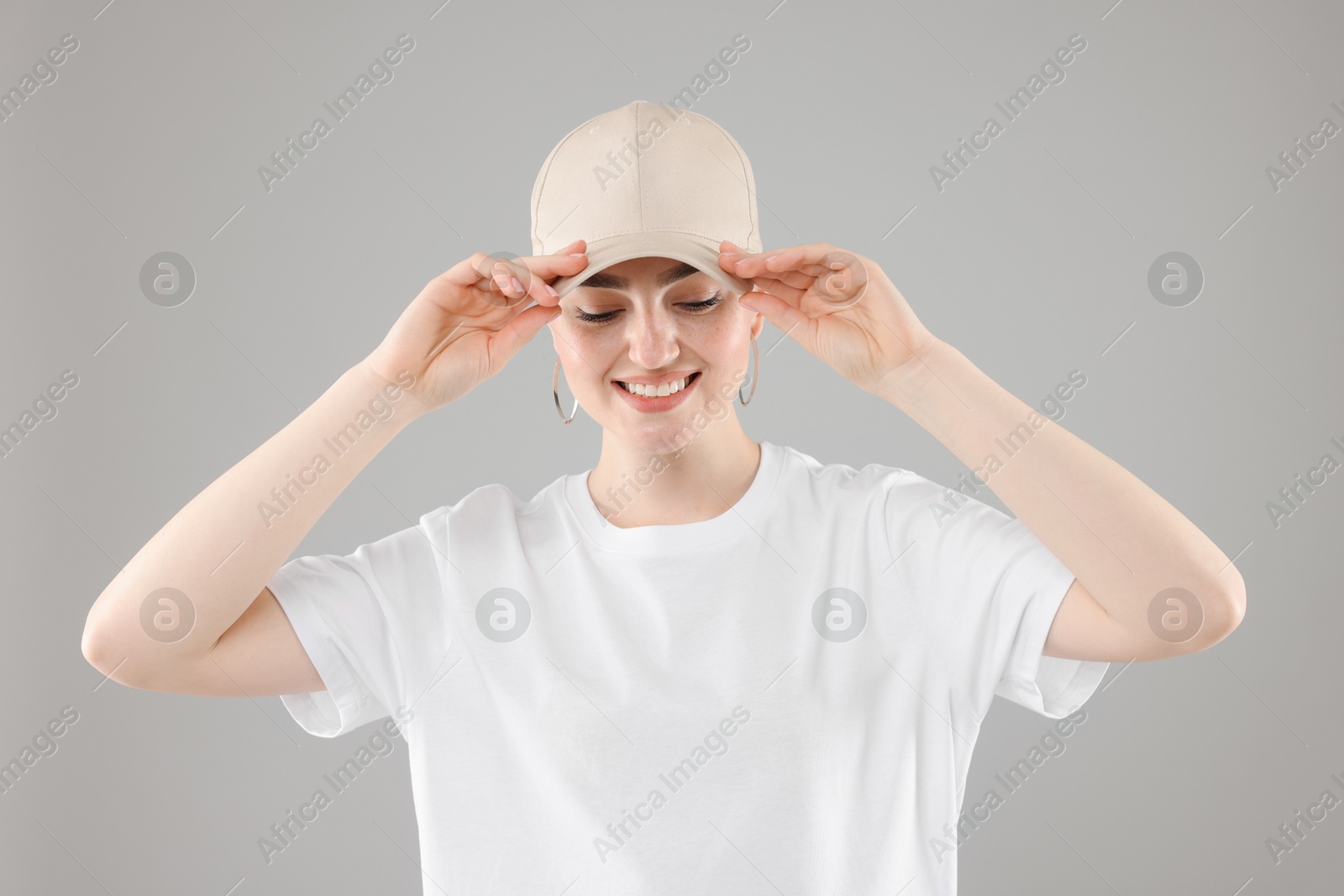Photo of Smiling woman in stylish baseball hat on grey background