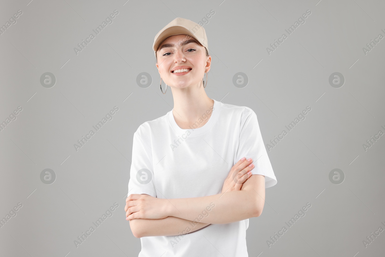 Smiling woman in stylish baseball hat on grey background Photo of Smiling woman in stylish baseball hat on grey background
