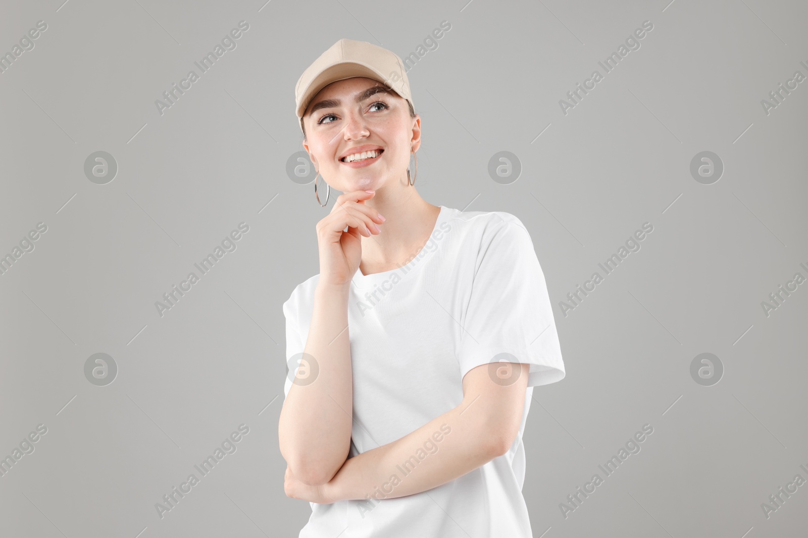 Smiling woman in stylish baseball hat on grey background Photo of Smiling woman in stylish baseball hat on grey background