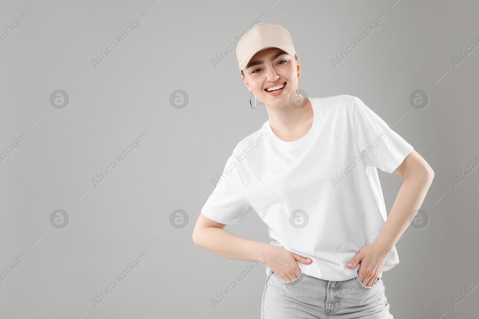 Portrait of smiling woman in stylish baseball hat on grey background. Space for text Photo of Portrait of smiling woman in stylish baseball hat on grey background. Space for text