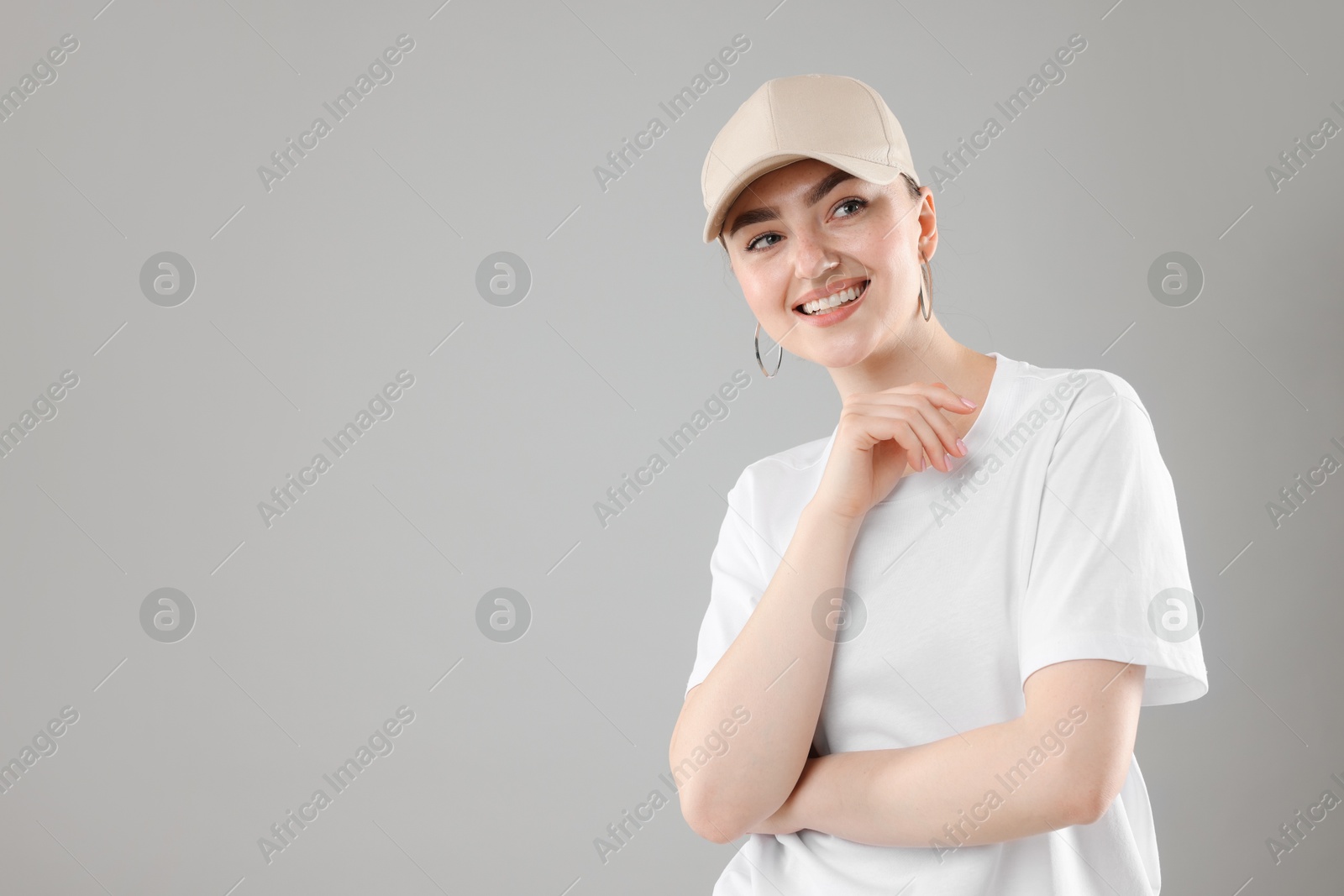 Portrait of smiling woman in stylish baseball hat on grey background. Space for text Photo of Portrait of smiling woman in stylish baseball hat on grey background. Space for text