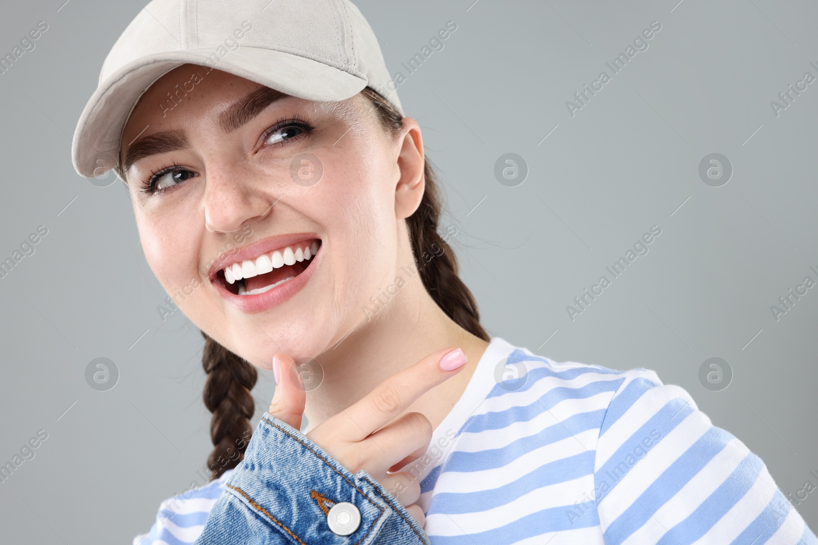 Happy woman in stylish baseball hat on grey background, closeup Photo of Happy woman in stylish baseball hat on grey background, closeup