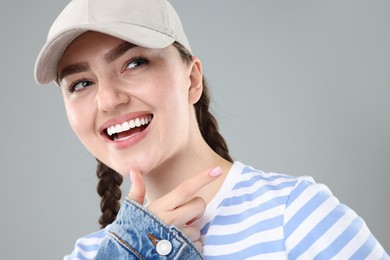 Photo of Happy woman in stylish baseball hat on grey background, closeup
