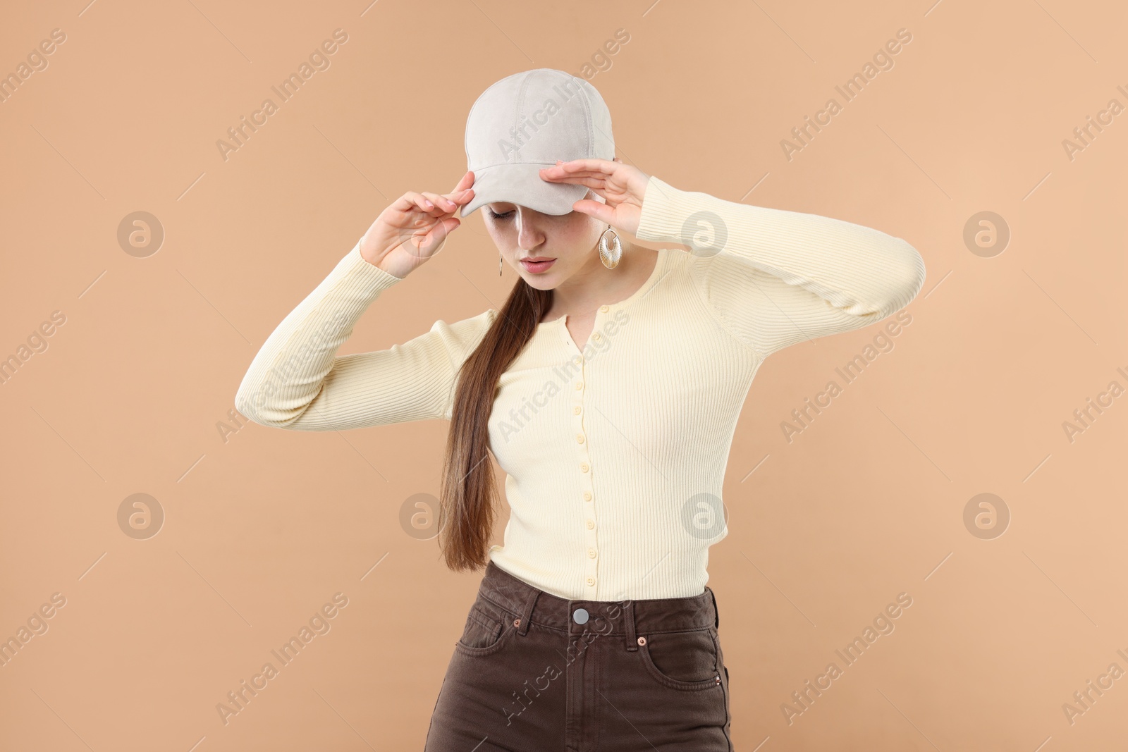 Beautiful woman in stylish baseball hat posing on beige background Photo of Beautiful woman in stylish baseball hat posing on beige background