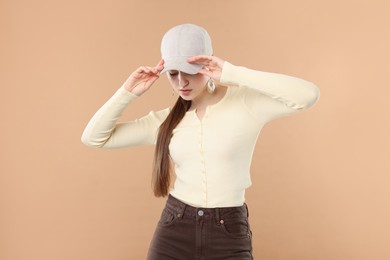 Photo of Beautiful woman in stylish baseball hat posing on beige background