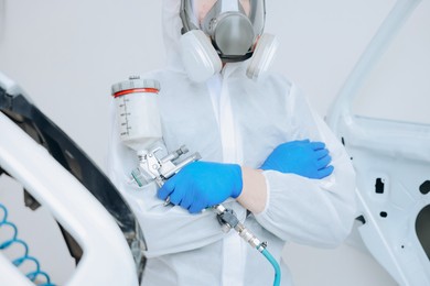 Photo of Worker with spray painting gun and car in body shop, closeup