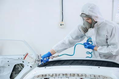 Photo of Worker spray painting car in body shop. Space for text