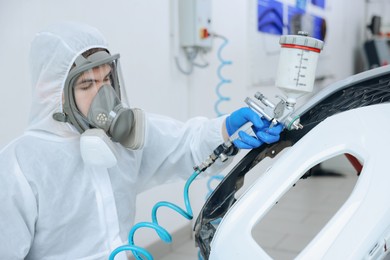 Photo of Worker spray painting car in body shop