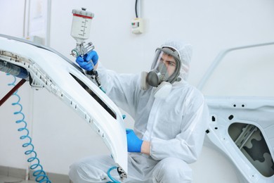 Photo of Worker spray painting car in body shop