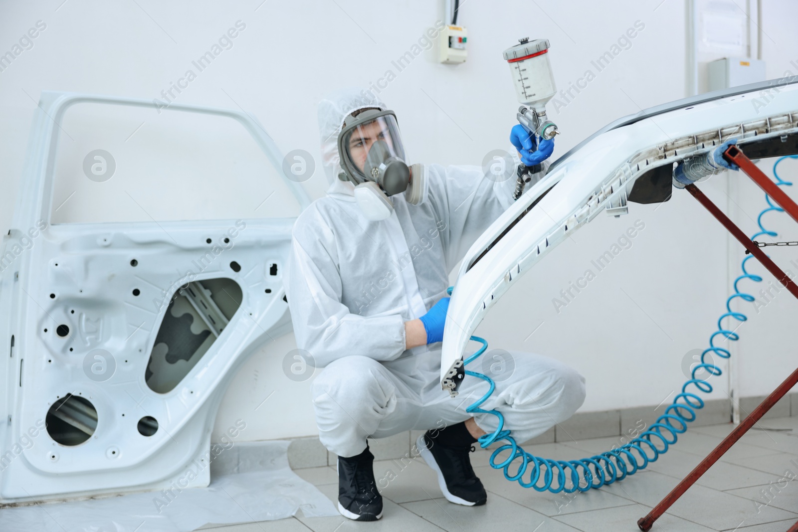 Worker spray painting car in body shop Photo of Worker spray painting car in body shop