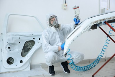 Photo of Worker spray painting car in body shop